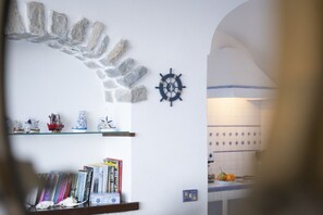 Eine Steinsäule mit Schiffsschwungrad, Regale mit Büchern und Dekoration, und ein Blick in eine Küche.