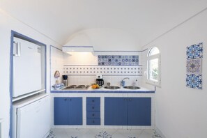 Eine kleine Küche mit blauen Schränken, weißen Geräten und Fliesen mit Muster.