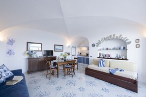 Ein Wohnzimmer mit Sofa, Esstisch mit Stühlen, Küchenzeile und einer eingebauten Bücherreol.