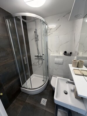 A modern bathroom with a glass-enclosed shower, a white sink, and a marble-tiled wall. - Cozy Stay for 2 in Sukosan (Sukosan)