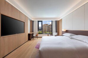 A hotel room with a large bed, a desk, a chair, a TV, and a window with a view of buildings. - La Quinta by Wyndham Lishui Yunhe (Lishui)