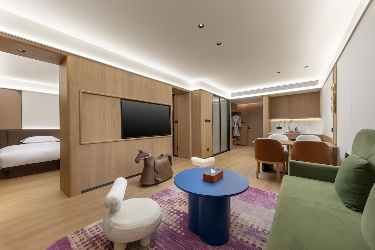 Quarto de hotel moderno com cama, área de estar e televisão.