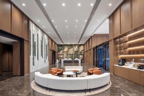 A hotel lobby with a reception desk, seating area, and a coffee station.