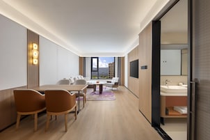 Habitación de hotel moderna con zona de comedor, sofá, televisión y baño.