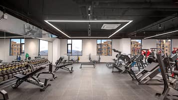 Une salle de sport moderne, dotée de divers appareils d’exercice, de grandes fenêtres et offrant une vue sur les bâtiments environnants.