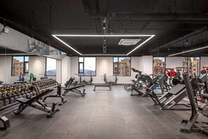 Uma academia moderna com diversos equipamentos de exercício, amplas janelas e vista para edifícios.