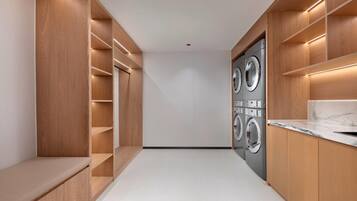 A modern laundry room with built-in washers and dryers, wooden shelving, and a marble countertop.