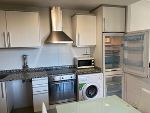 A compact kitchen with a stove, microwave, oven, and washing machine. - BEACH APARTMENT IDEAL FOR COUPLES AND FAMILIES (Peñíscola)