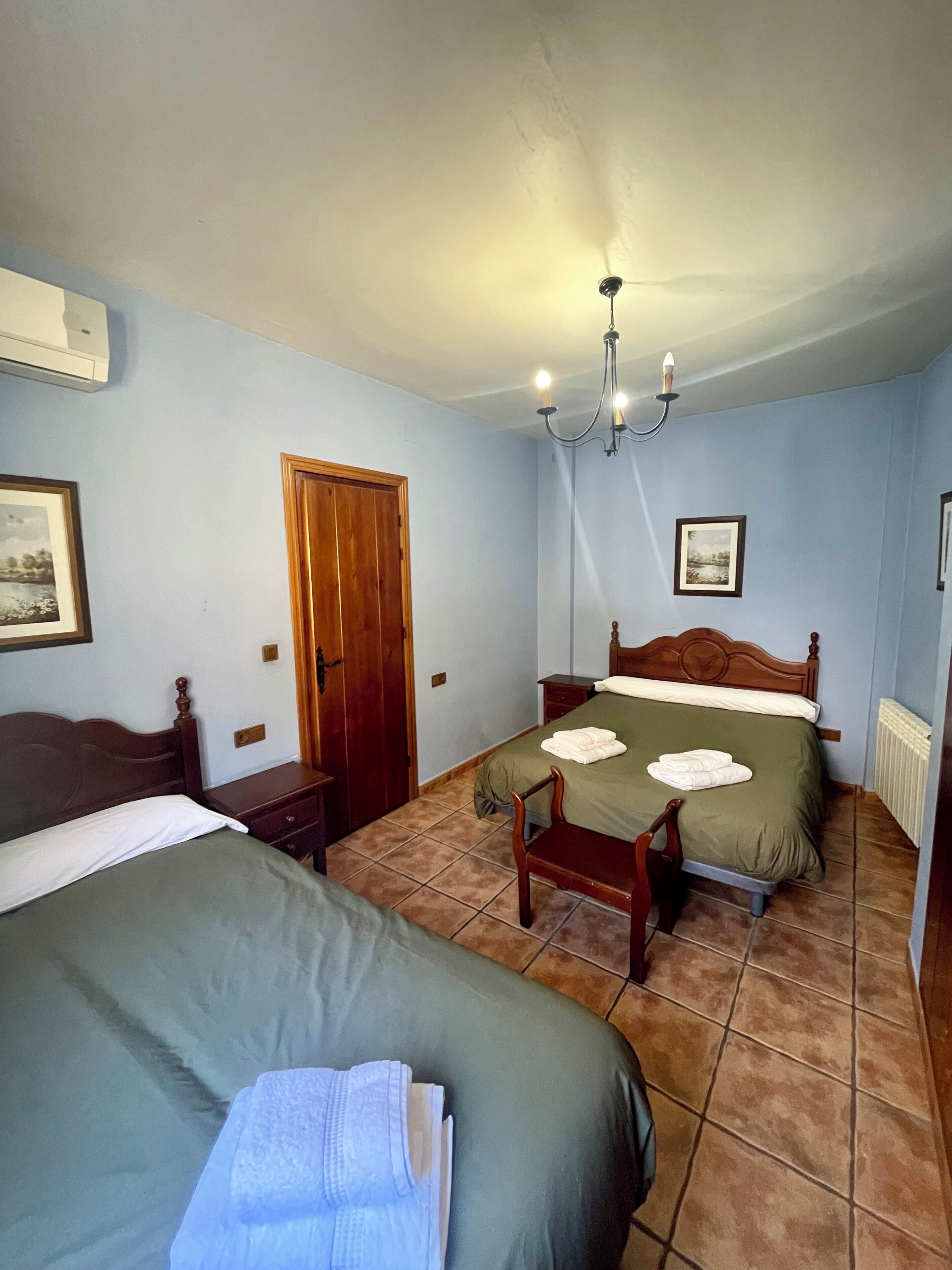 Un dormitorio con dos camas, una puerta de madera, un radiador y una araña.