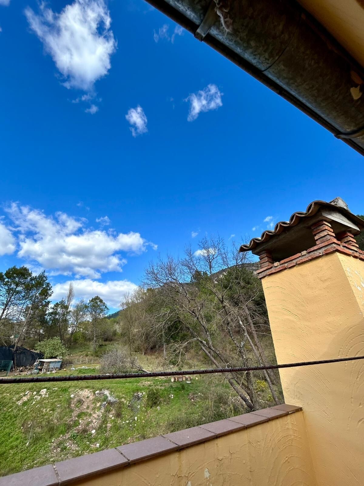 A view of a yellow building with a tiled roof, surrounded by trees and a clear blue sky.