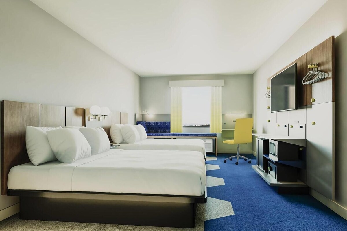 A hotel room with two beds, a desk, a chair, a TV, and a window with a view.