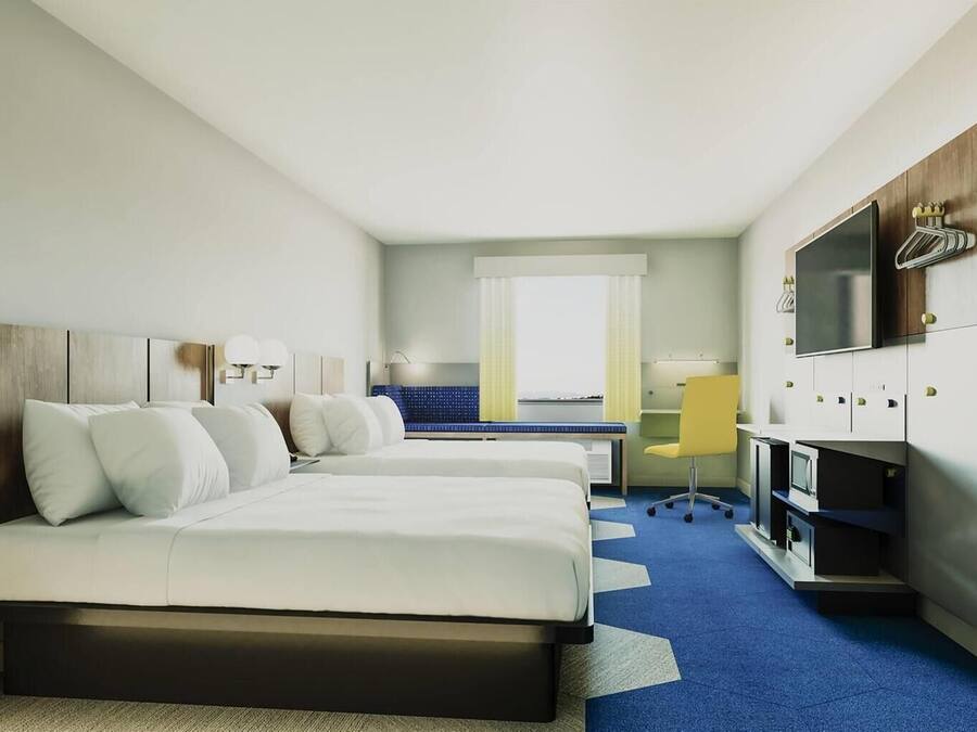 A hotel room with two beds, a desk, a chair, a TV, and a window with a view.