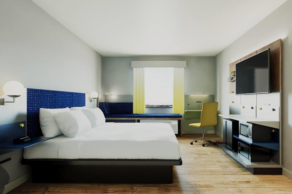 A hotel room with a bed, a desk, a chair, a TV, and a minibar.