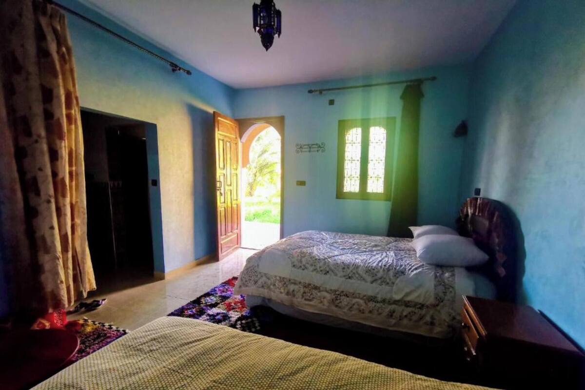 A bedroom with a bed, a window, a door, and a hanging light fixture.