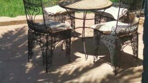 A patio with a round table and four chairs, surrounded by lush greenery and palm trees.