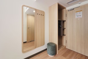 A room with a large mirror, a wooden wardrobe, a small stool, and a door with a notice.