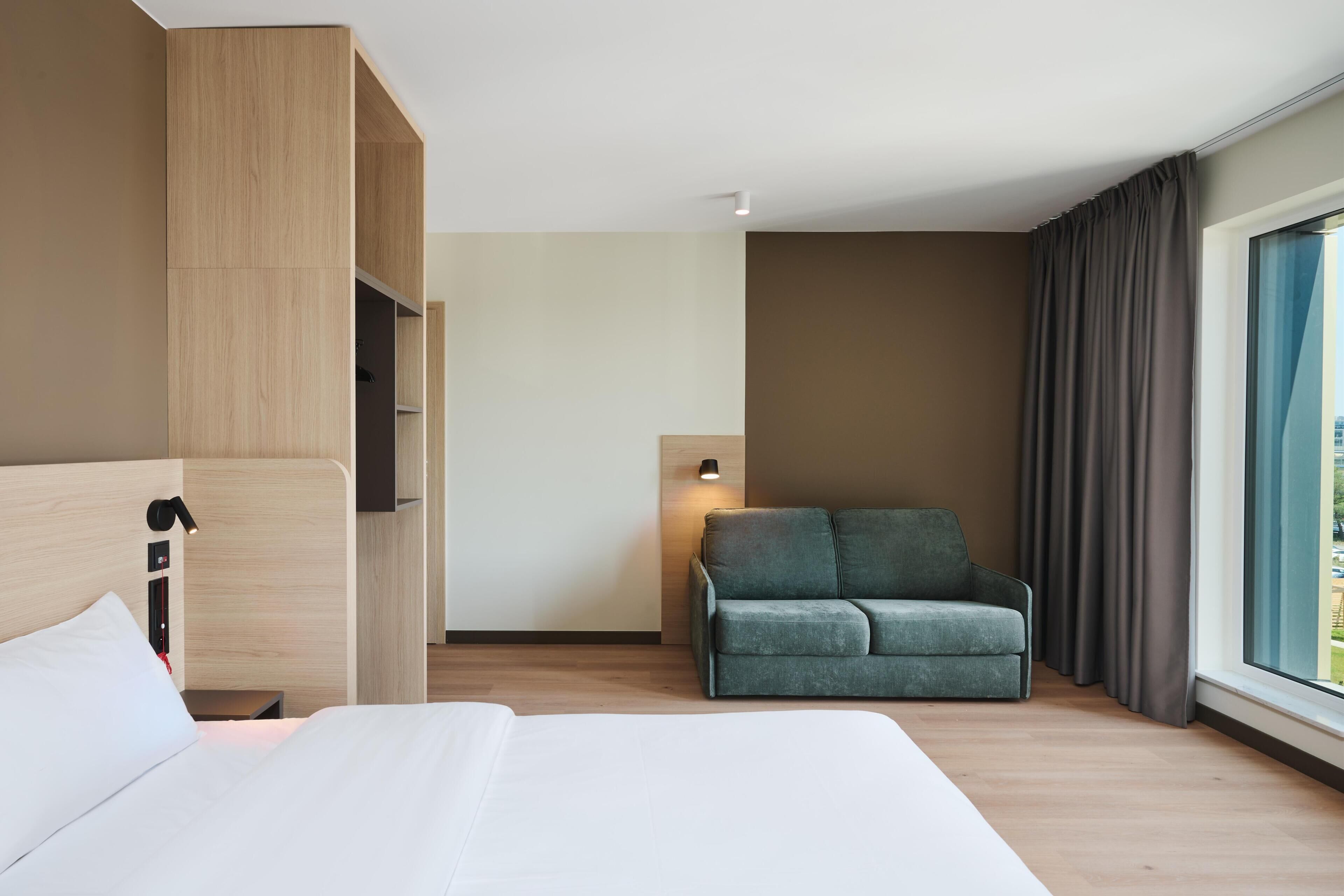 A hotel room with a bed, a seating area, a desk, and a window with curtains.