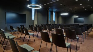 A conference room with rows of chairs, a large screen, and ceiling lights.