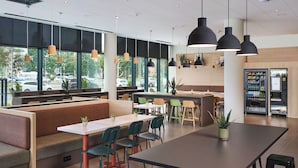 A modern cafe interior with seating arrangements, pendant lighting, and a vending machine.