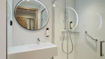 Un baño moderno con ducha envuelta en vidrio, un espejo redondo y un lavamanos blanco.