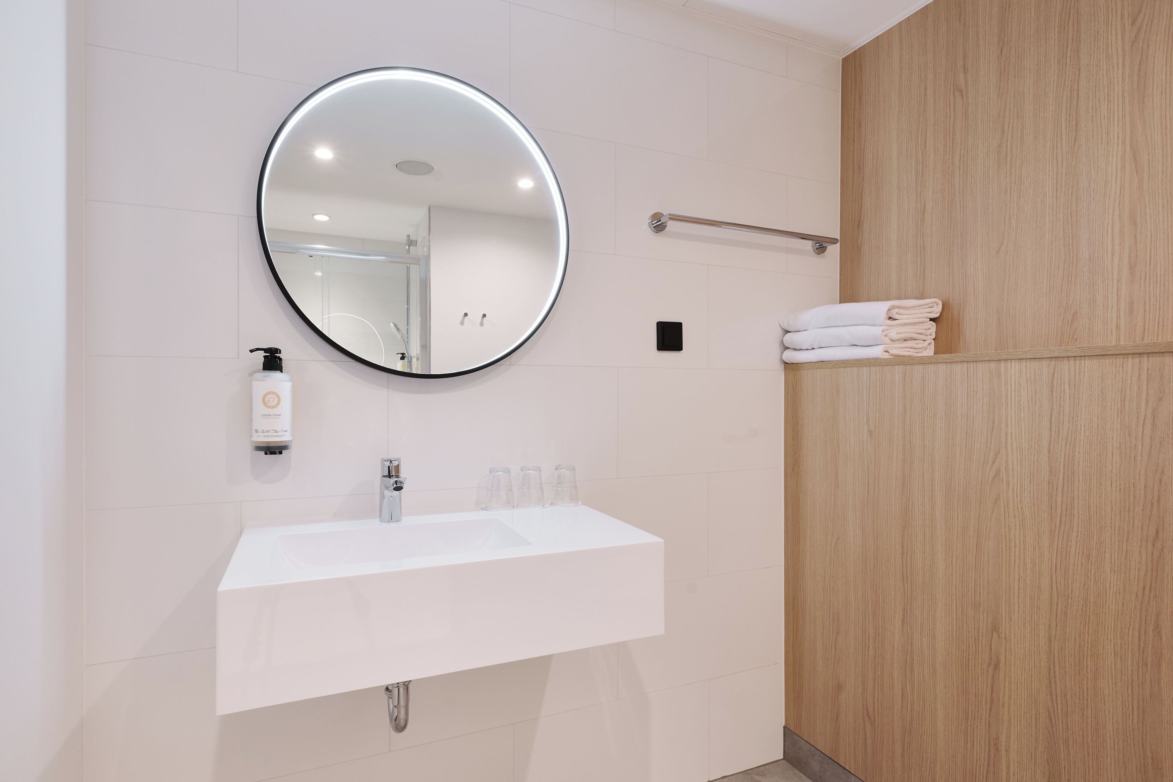 A modern bathroom with a round mirror, white sink, and wooden paneling.