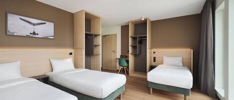 Hotellihuone, jossa on kolme sänkyä, työpöytä ja vaatekaappi.