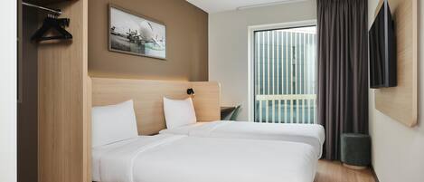 Ein Hotelzimmer mit zwei Betten, einem großen Fenster mit Vorhängen, einem flachbildfernseher an der Wand und einem gerahmten Bild.