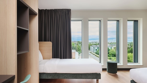 A modern hotel room with a bed, a view of the city, and a large window.