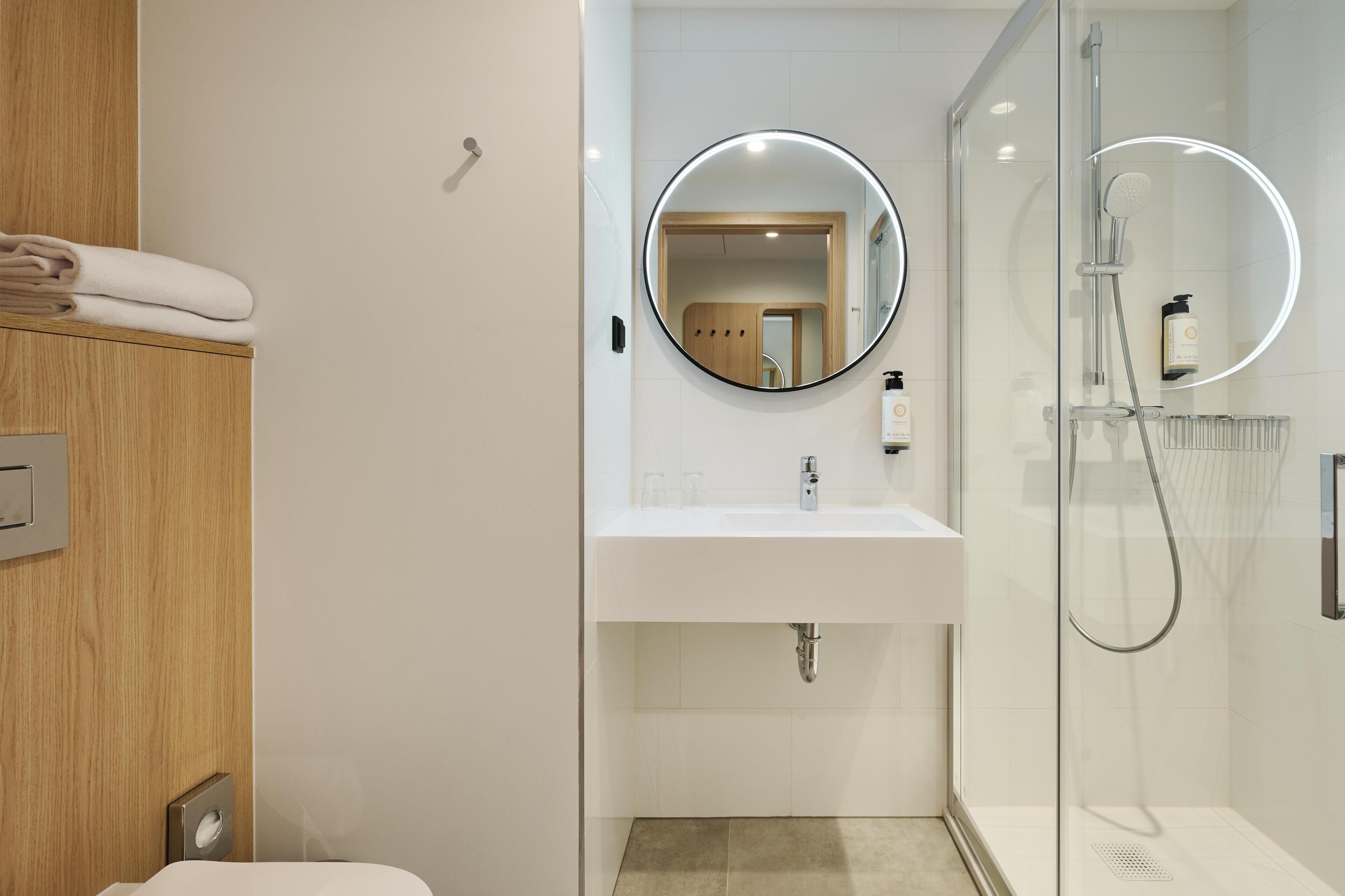 Une salle de bain moderne avec une douche à parois de verre, un lavabo blanc et un miroir rond.