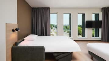 Habitación de hotel moderna con una cama grande, una mesita de noche, un televisor de pantalla plana y vistas a la ciudad a través de las ventanas.