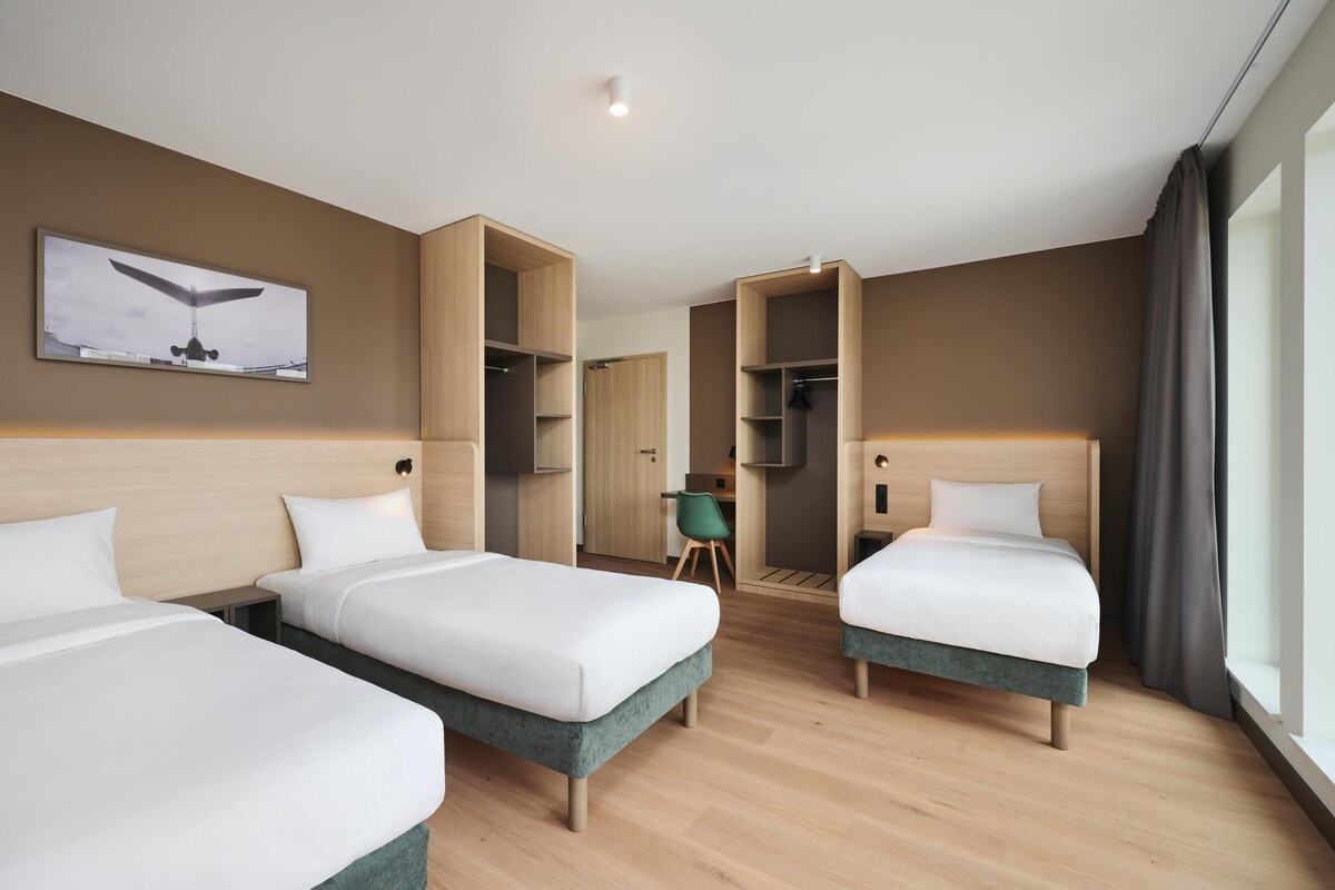A hotel room with two single beds, a desk, a chair, and a wardrobe.