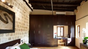 Un dormitorio con una cama grande, almohadas verdes, cabecera de madera, pared de piedra y un armario de madera oscura.