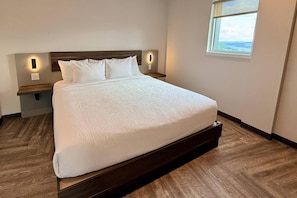 Una cama bien tendida con un cabecero de madera y dos mesitas de noche con lámparas de pared.