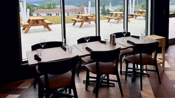 Restaurante con amplios ventanales que ofrece vistas a mesas de picnic y al campanario de una iglesia.