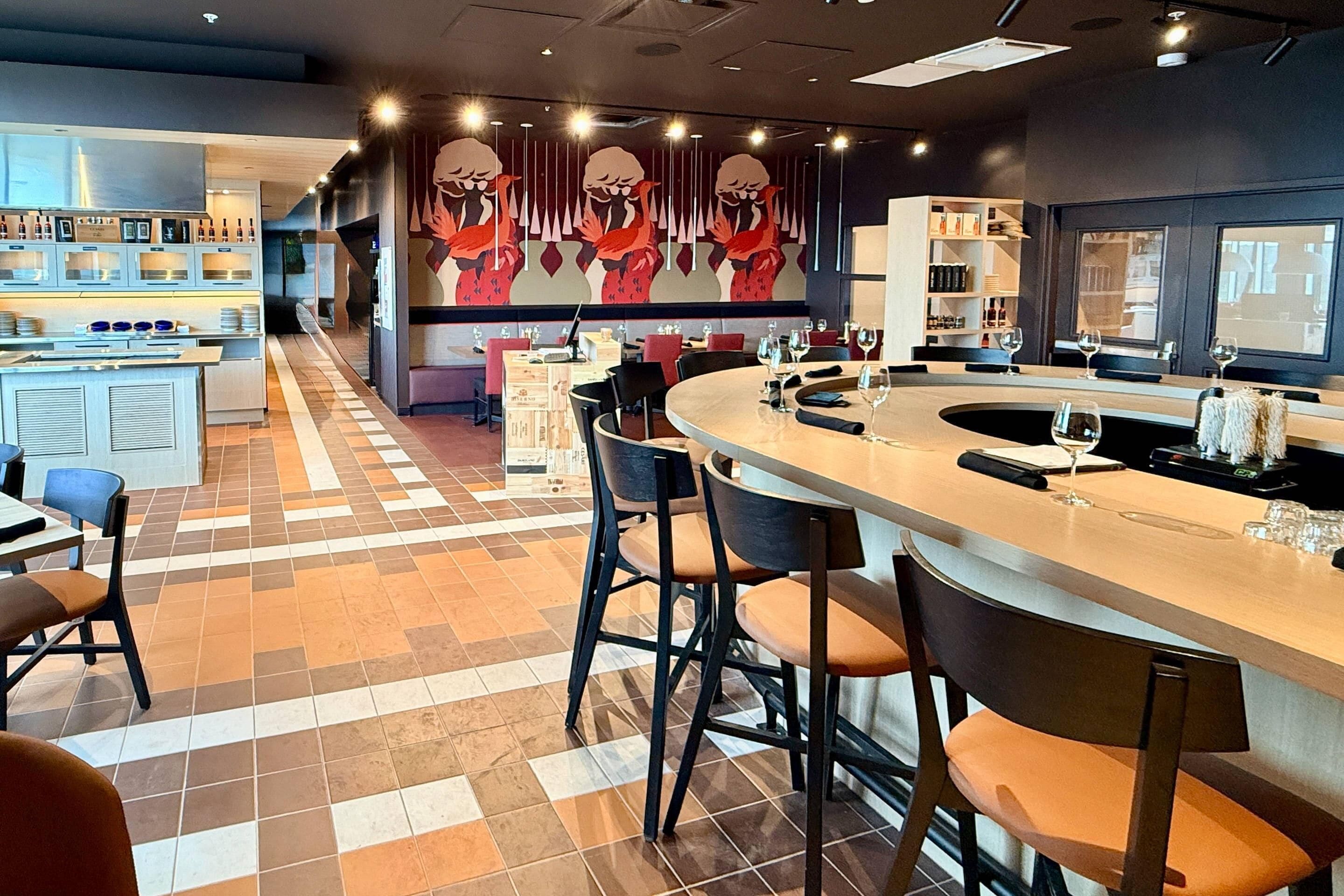 A modern bar area with a checkered floor, bar stools, and a counter with glasses.