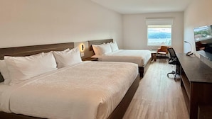 Habitación de hotel con dos camas, un escritorio, una silla y un televisor.