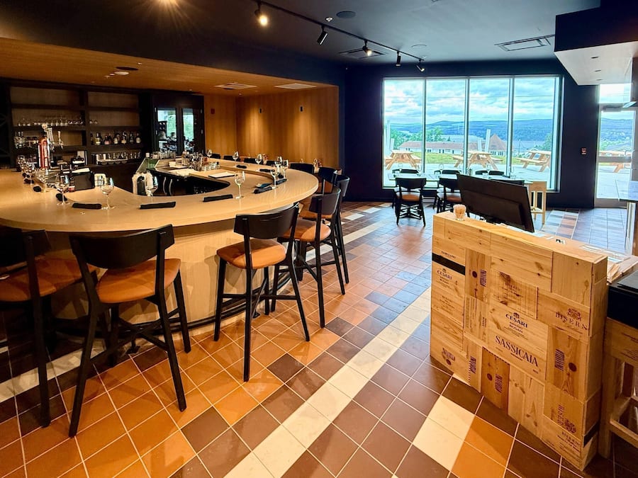 Un bar moderno con barra curva, diversas opciones de asientos y vistas al exterior a través de amplios ventanales.