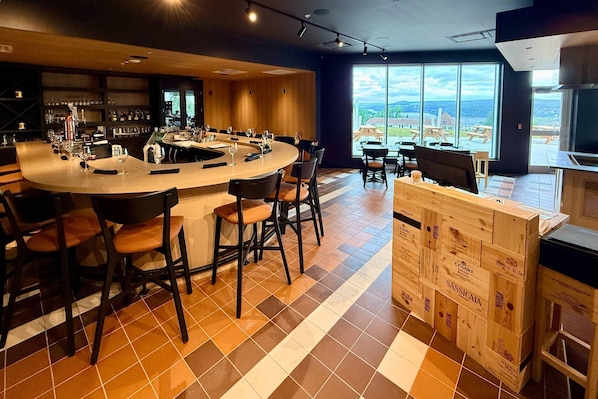 Un bar moderno con barra curva, diversas opciones de asientos y vistas al exterior a través de amplios ventanales.