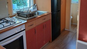 Cocina compacta con estufa a gas, horno, pileta y refrigerador negro.