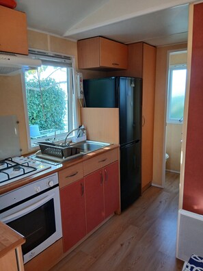 A compact kitchen with a gas stove, oven, sink, and a black refrigerator. - Rental MH/2bedrooms/4pers/air-conditioned/terrace enclosed parking in Balaruc les bains (Balaruc-les-Bains)