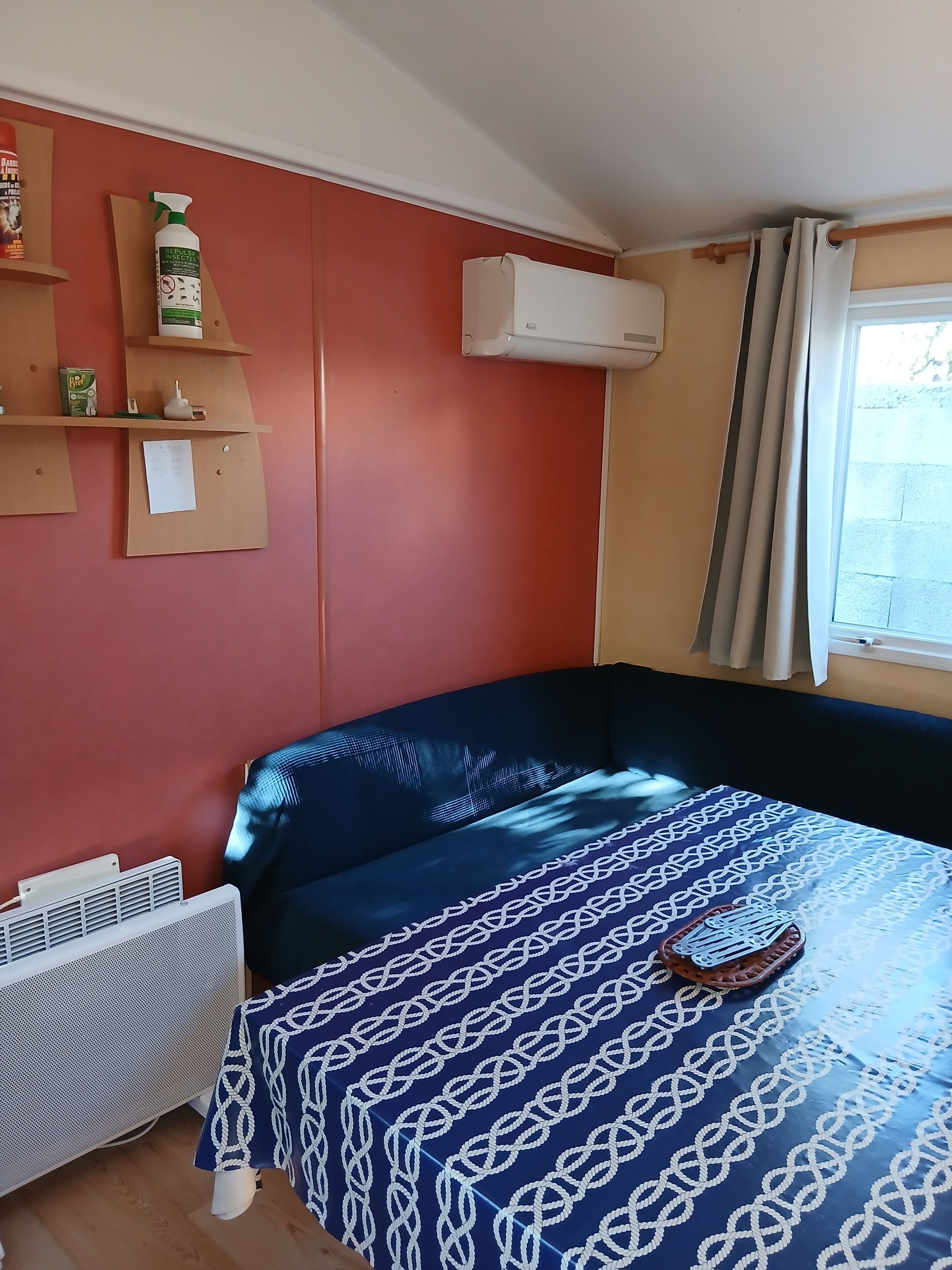 A room with a bed, a radiator, a shelf with items, and a window with curtains.