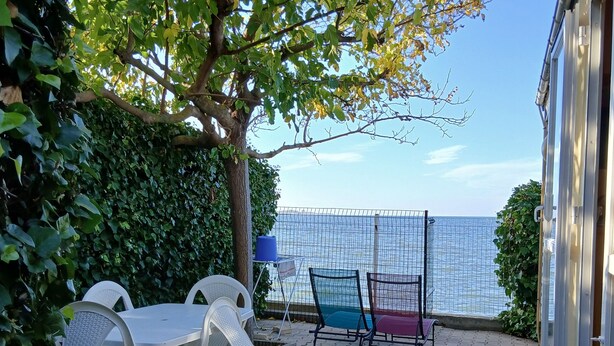 Un patio con mobiliario exterior, un árbol y vista al mar.