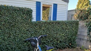 Una bicicleta estacionada frente a una casa con seto, suelo de grava y una rejilla metálica.