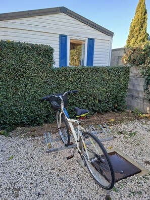 A bicycle parked in front of a house with a hedge, gravel ground, and a metal grate. - Rental MH/2bedrooms/4pers/air-conditioned/terrace enclosed parking in Balaruc les bains (Balaruc-les-Bains)