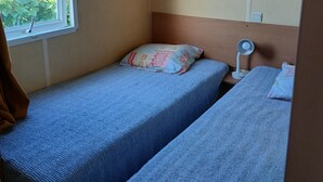 Una habitación pequeña con dos camas, una ventana con vista al mar y una mesita de noche con lámpara.