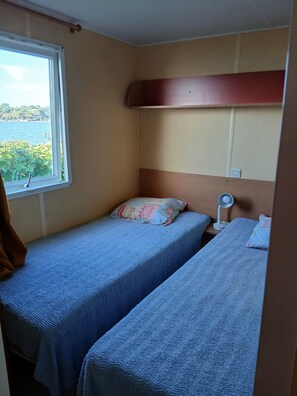 A small room with two beds, a window with a view of the sea, and a bedside table with a lamp. - Rental MH/2bedrooms/4pers/air-conditioned/terrace enclosed parking in Balaruc les bains (Balaruc-les-Bains)