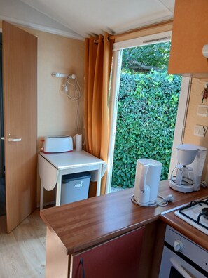 A compact kitchenette with a stove, coffee maker, and a small table with a microwave. - Rental MH/2bedrooms/4pers/air-conditioned/terrace enclosed parking in Balaruc les bains (Balaruc-les-Bains)