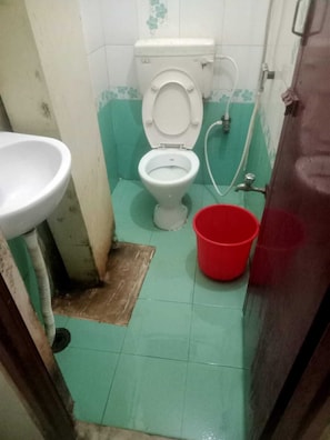 A small bathroom with a toilet, a sink, and a red bucket. - MN Guest House (Chennai)
