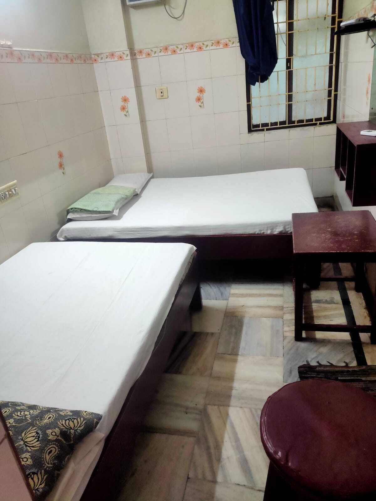 A room with two single beds, a wooden bench, a small table, and a window with bars.