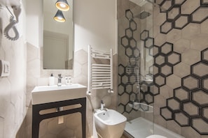 A modern bathroom with a white sink, black pedestal, and a glass shower enclosure. - Five Boutique Rooms (Naples)